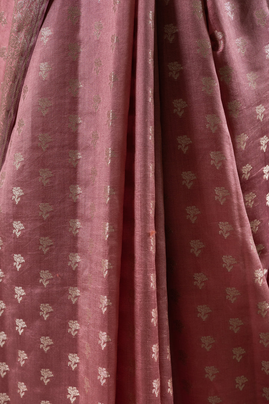A close-up of dusty rose pink fabric with small metallic gold floral motifs woven all over, showing the texture and drape of the material.